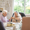 A group of older people sit within a communal area enjoying refreshments and chats