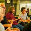 A group of older people enjoy a community social group taking part in seated movement exercises.