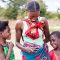 A mother and two young children in rural Zambia, using a mobile phone to give feedback to Loop.