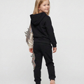 PDP image generated with On-Model.com A smiling young girl in a black hoodie with colorful feather designs on the sleeves and pants, standing barefoot