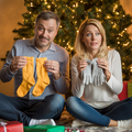 A Photo of a couple on Christmas morning sitting under a tree having gifted each other socks and gloves. 