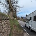 A road with a caravan driving down it and little  space for anyone to walk safely.