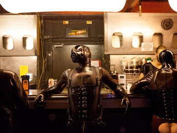 Man leaning on a bar in a gas mask and full latex body suit. Photo by Paul Soso.
