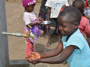 Child at a preschool washing their hands with a pump installed and maintained by Pump Aid