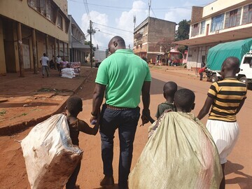 S.A.L.V.E. International staff member with children who are on the streets of Jinja, carrying bags of scrap that they have collected as a means of inc
