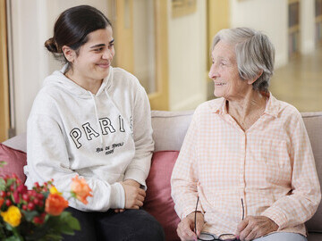 Smiling young woman sat down by the side of a smiling older lady
