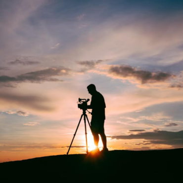 A photograph of a man filming at sunset. 