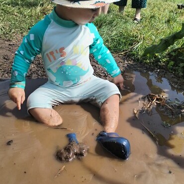 A young boy sits in a muddy puddle looking for worms